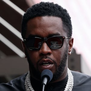 Sean Combs speaks behind a microphone and clear podium outdoors.