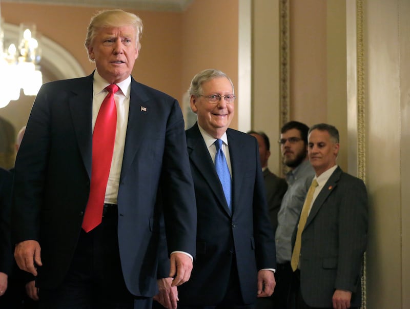 Donald Trump walks in front of a smiling Mitch McConnell.