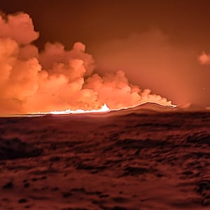 A local resident watch smoke billow as the lava colour the night sky orange from an volcanic eruption on the Reykjanes peninsula 3 km north of Grindavik, western Iceland on December 18, 2023. 