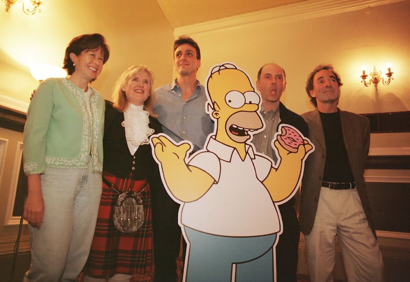 A still of a 90s episode of The Simpsons shows the entire Simpsons family posing outside of their house.