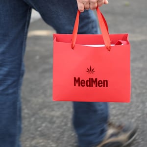 A photo of a MedMen customer carrying a red MedMen shopping bag.