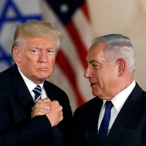 Donald Trump and Benjamin Netanyahu clasp hands together.