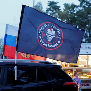 A flag of the Wagner Group’s logo waving in front of a Russia flag.