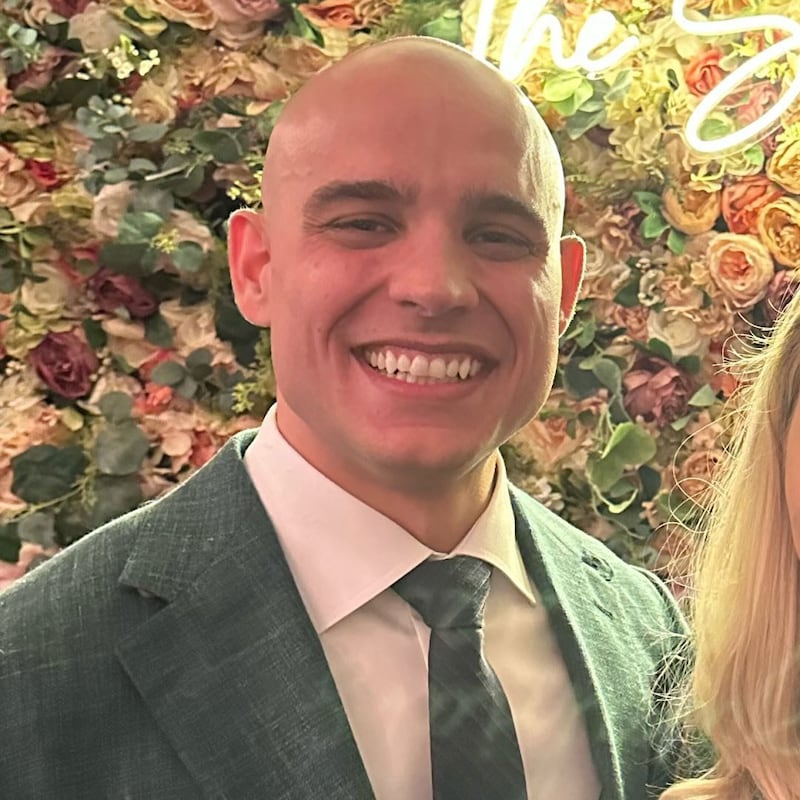 James Blair grinning in front of a Christmas tree or flower wall