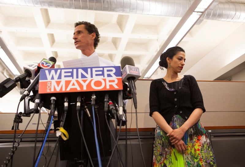 Huma Abedin looks down while standing next to her then-husband at a press conference.