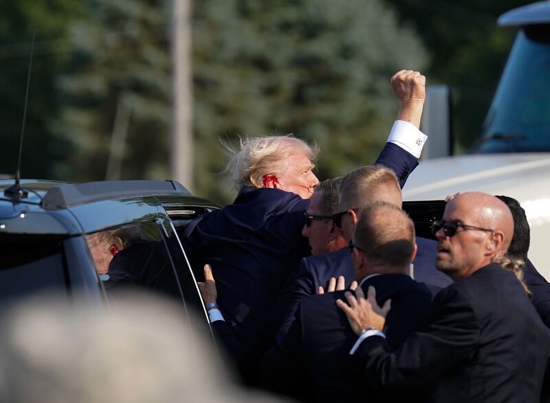 Former president Donald Trump raises his arm as he's helped into a Secret Service vehicle after an assassination attempt