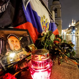 People walk past a portrait of Russian military blogger Vladlen Tatarsky, who was killed in a cafe explosion, with St. Basil’s Cathedral in the background in Moscow, Russia, April 4, 2023.