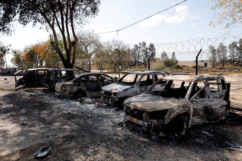 Burnt cars sit in a line in front of a barbed wire fence.