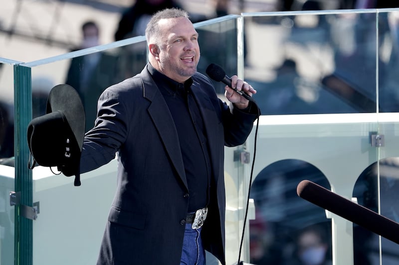 Garth Brooks sings outdoors while holding a black cowboy hat