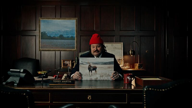 Matty Matheson sits at a desk holding a picture of a moose.