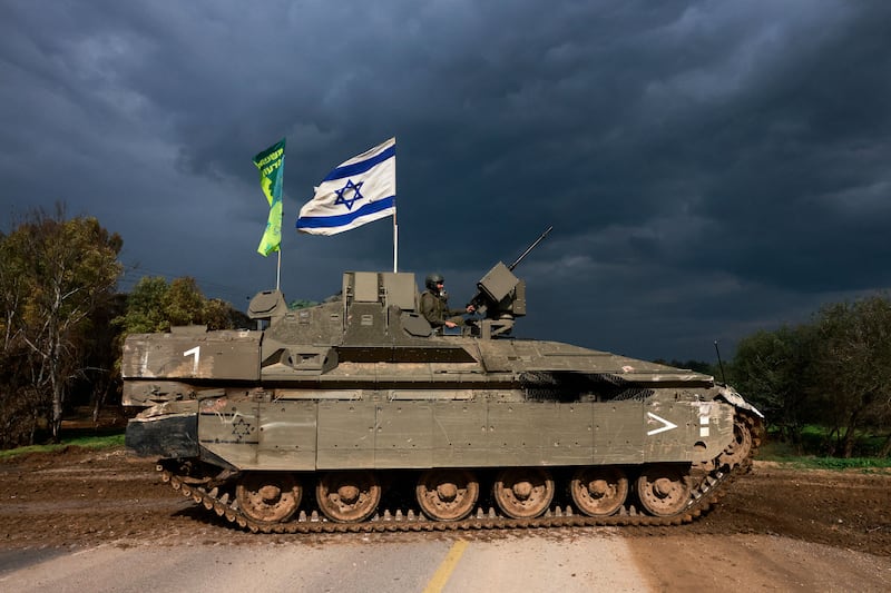 A picture of a tank with an Israeli flag flying on top of it rolls across a street in Gaza.