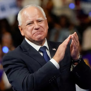 Tim Walz smirks and claps on stage at a rally.