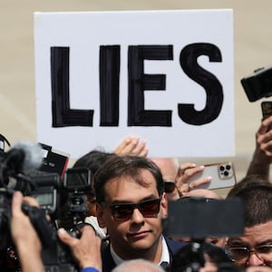 A picture of Rep. George Santos leaving court as a protester holds up a sign reading, “LIES”