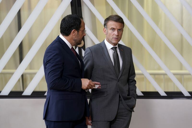 France's president, Emmanuel Macron, looking downcast in front of a glass wall with a man to his left talking to him