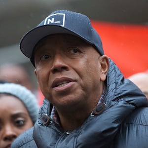 Russell Simmons, wearing a hat, prepares to speak at an outside event.