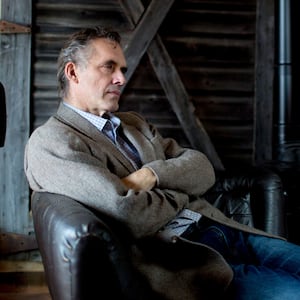 Jordan Peterson sits in a chair with his arms crossed