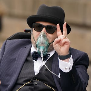 Nicholas Rossi throws up a peace sign as he is wheeled out of court in 2022.