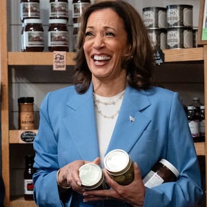 Kamala Harris holding two jars of food and talking to a man with his back to camera in an artisanal food store