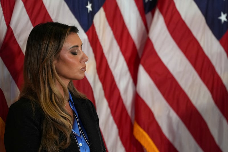 Alina Habba shuts her eyes with American flags in the background.