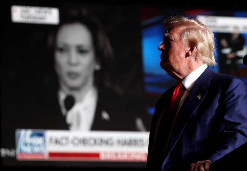 Donald Trump appears in the foreground with Harris on a TV screen in the background.