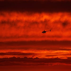 A helicopter travels south along the coast after sunset over the ocean as Hurricane Hilary approaches Del Mar, California.