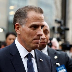 Hunter Biden stares forward while reporters with microphones surround him.