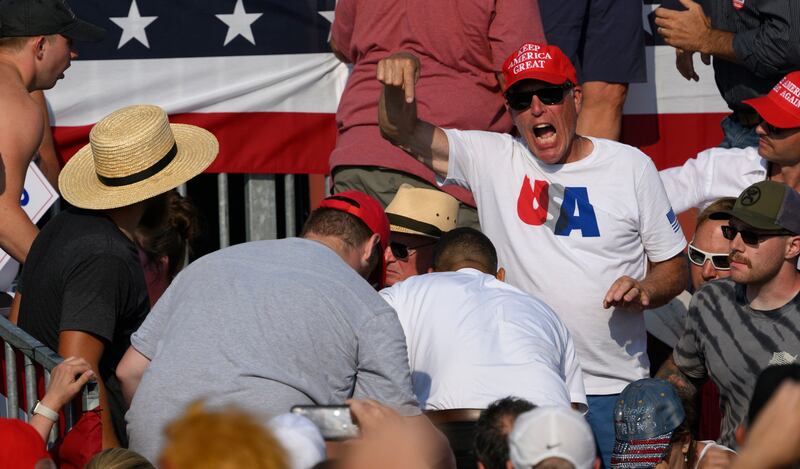 A man in a MAGA hat points down at an apparently wounded person at the Trump rally