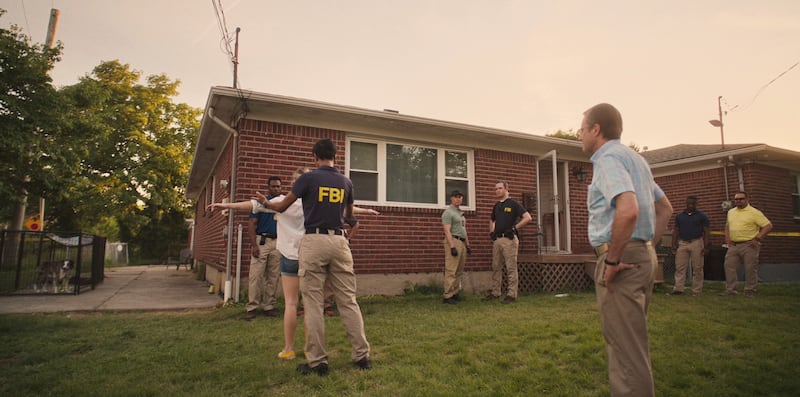 Screenshot of a scene in the film "Reality" with FBI searching folks on front lawn of house.