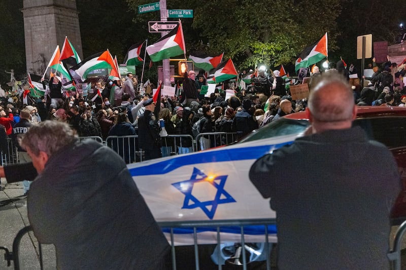 A picture of counter protestors holding an Israeli flag across the street where pro-Palestinian protesters gather for a march. 