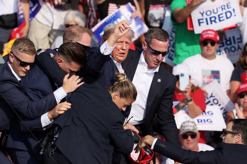 Donald Trump holds up a fist with his face bloodied as Secret Service agents rush him off stage.