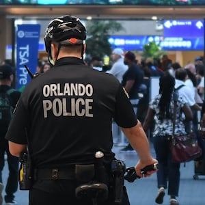 Police officers watch as travelers make their way through a TSA screening line at Orlando International Airport in July 2022.