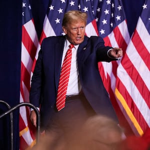 Donald Trump points into the crowd as he walks off stage in a suit at an event.