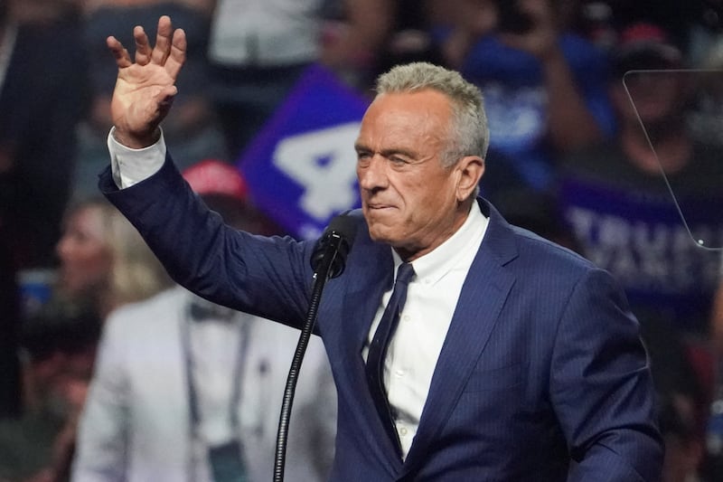 Robert F. Kennedy raises his hand while a crowd of Donald Trump supporters cheer.