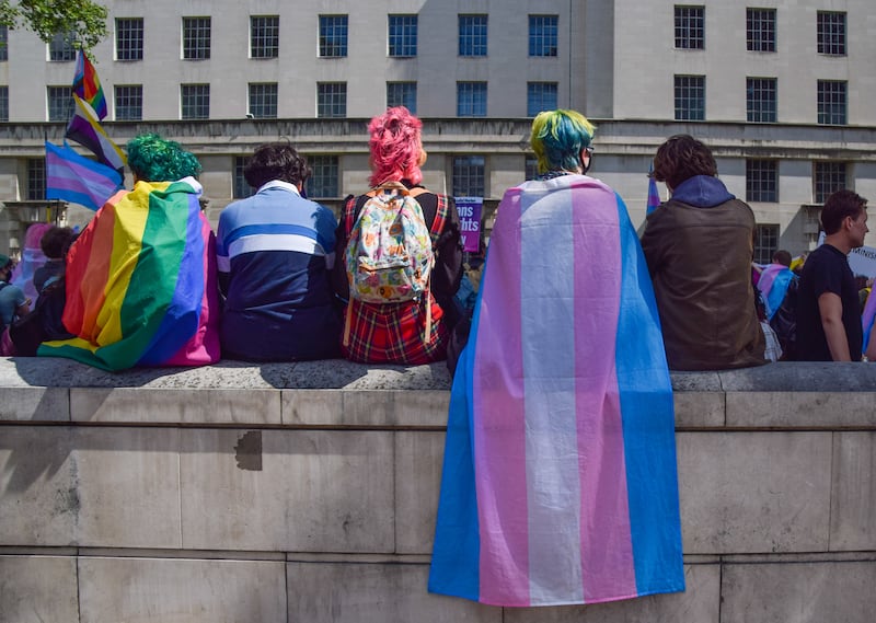 Protesters wrapped in pride and trans pride flags sit on a wall during the trans rights demonstration outside Downing Street in London.