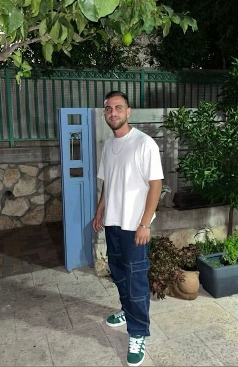 A picture of a smiling Itay Glisko in jeans, t-shirt, and green Adidas sneakers.