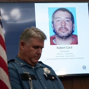 A police officer stands next to a screen displaying the picture of the suspected shooter, during a press conference following the deadly mass shooting, at City Hall in Lewiston, Maine.