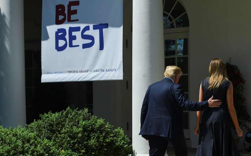 Melania Trump with Donald in front of a Be Best sign outside the White House. His hand is on her back.