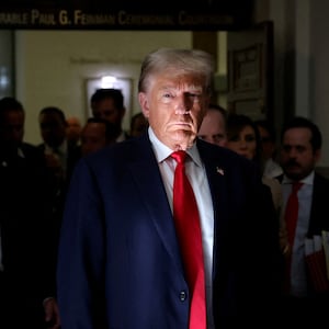 Donald Trump, wearing a suit and red tie, stares forward. 