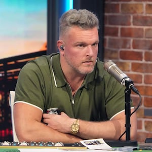 Pat McAfee sits in a green polo while sitting in front of a microphone for his show.