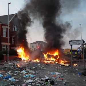 Riot police hold back protesters near a burning police vehicle after disorder broke out on July 30, 2024 in Southport, England. 