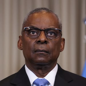 Lloyd Austin, wearing glasses and a suit, stares forward blankly.