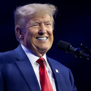 Donald Trump smiles on stage in front of a podium.