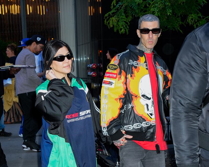 Kourtney Kardashian and Travis Barker wearing brightly colored jackets while holding hands on the sidewalk.