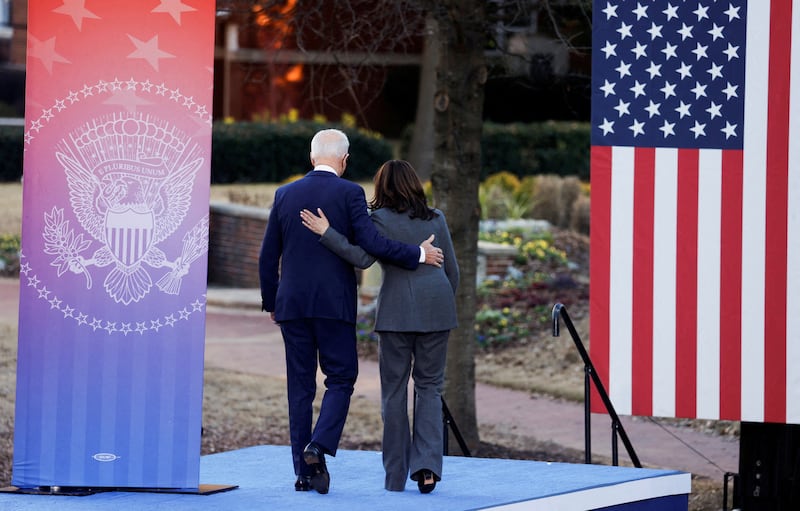 Seen from behind Joe Biden and Kamala Harris walking off a stage with Biden's hand on Harris' back