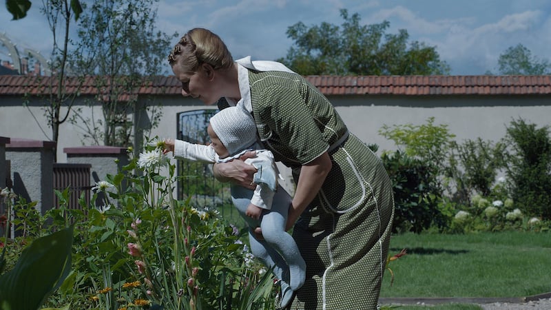 Sandra Huller holding a baby who is touching a flower in a still from ‘Zone of Interest’