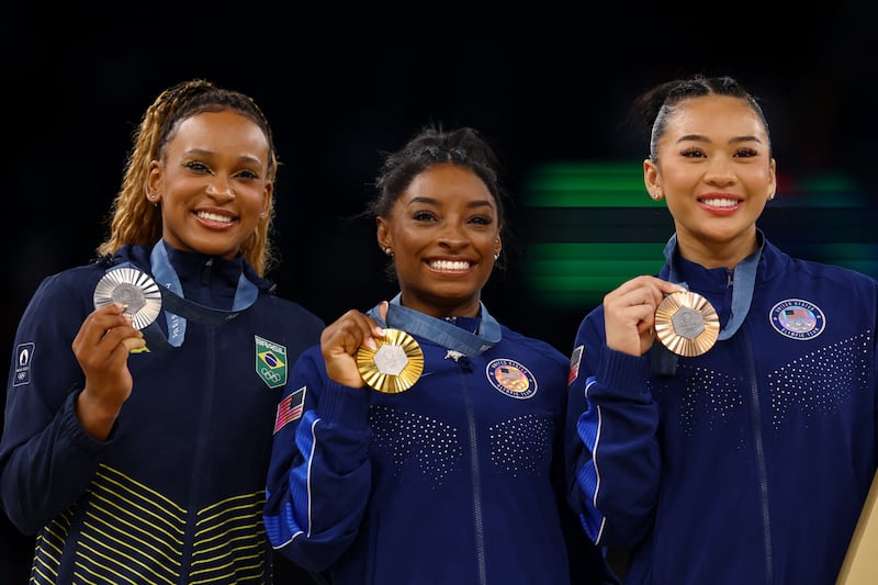 Simone Biles, Rebeca Andrade, and Sunisa Lee pose together.