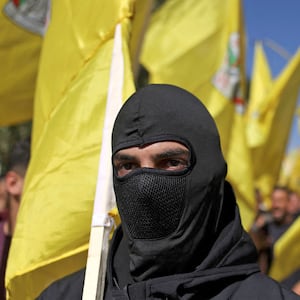 A photo of a man in a black mask in front of a crowd of Palestinians waving the yellow Fatah flag at a protest