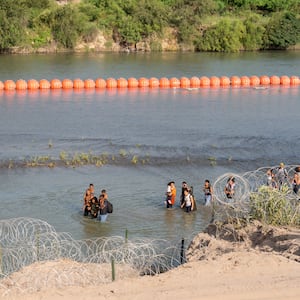 Migrants walk by a string of buoys placed on the water along the Rio Grande border with Mexico in Eagle Pass, Texas.