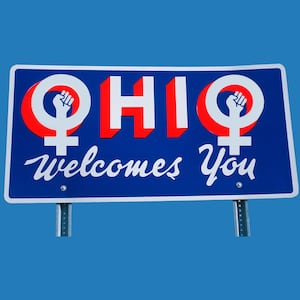 A photo illustration of an Ohio state road sign with women’s empowerment symbols.