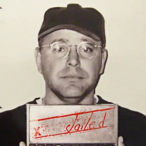 Tim Walz in a mugshot wearing a baseball cap and glasses